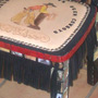 A chair with mosaic tiles, a tooled leather seat and black fringe along the apron